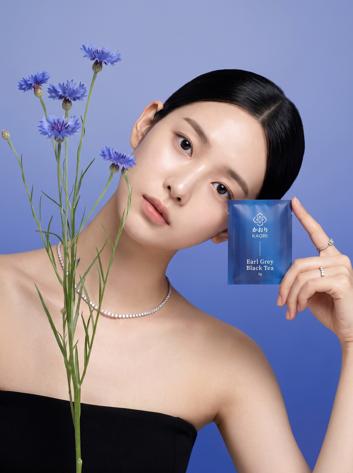 A woman at the edge of a bright blue pool, laughing and holding up the Kaori Earl Grey Black Tea pouch
