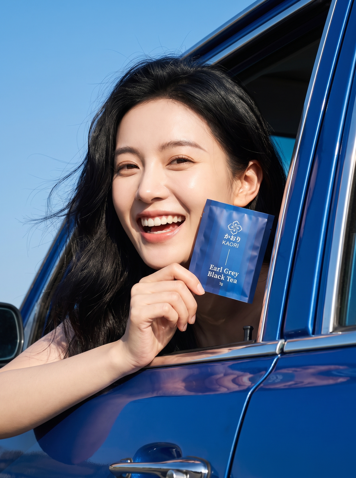 A woman leaning out of a red vintage car against a burgundy wall, laughing and holding up the Kaori Assam Black Tea pouch