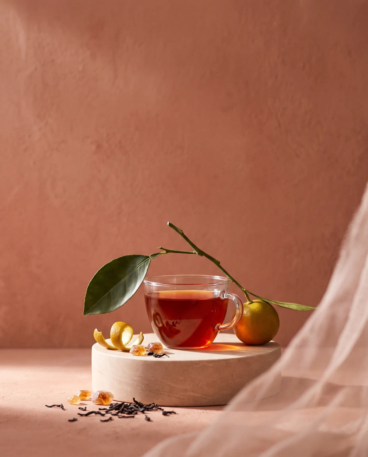 A cup of deep amber-red black tea on a pale plinth, a bergamot branch above it