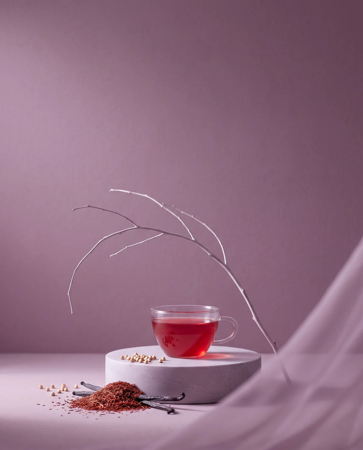 A cup of ruby-red rooibos on a pale plinth, a bare branch arcing above it