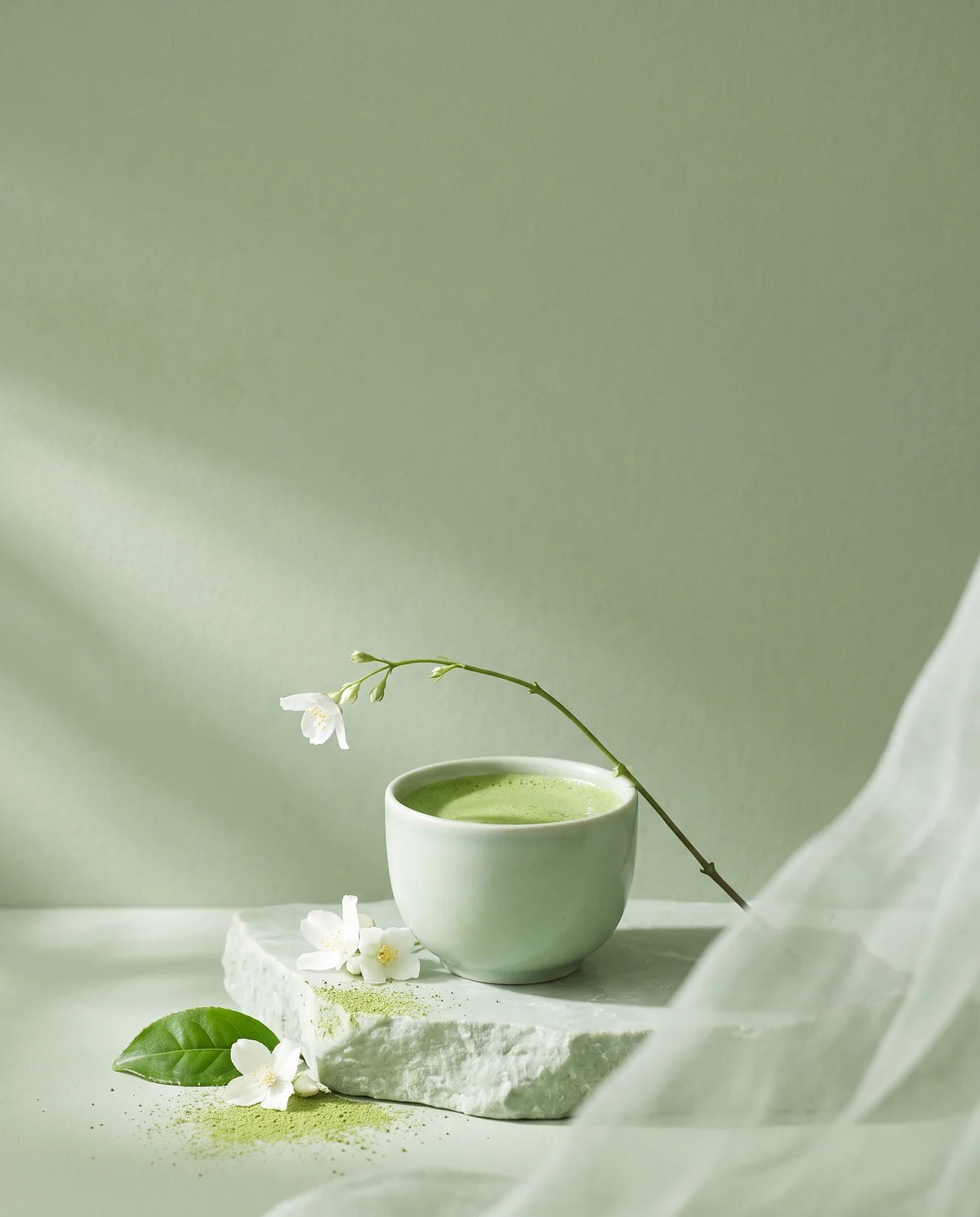 A cup of jade-green tea on a pale plinth, jasmine blossom arcing above it