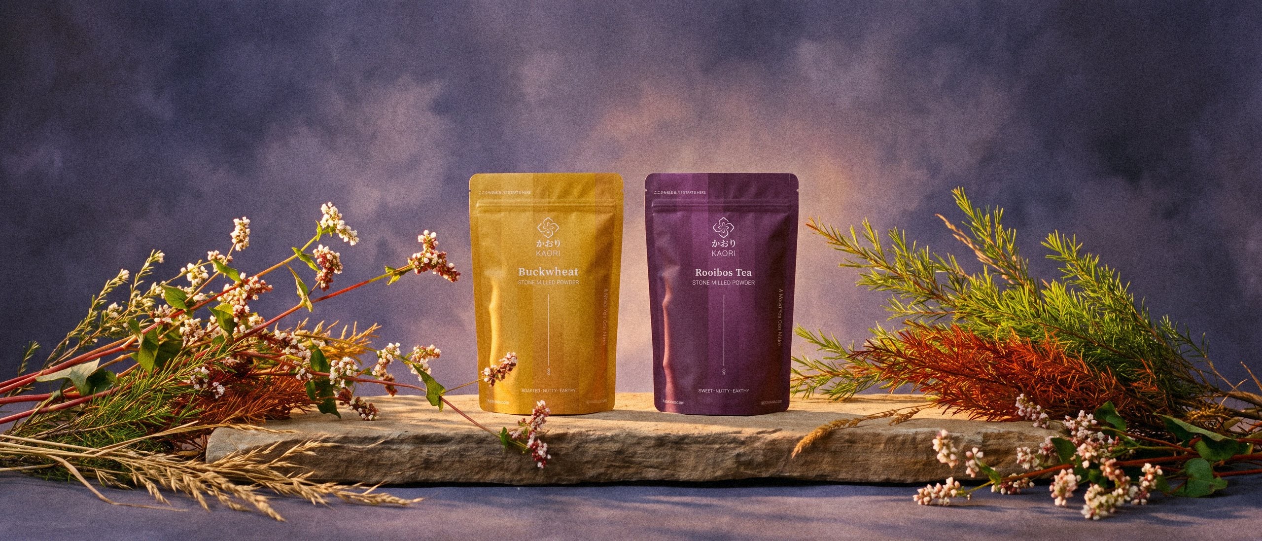 Buckwheat and Rooibos pouches on a long sandstone slab between flowering buckwheat and rooibos branches, before a dusk violet painted backdrop