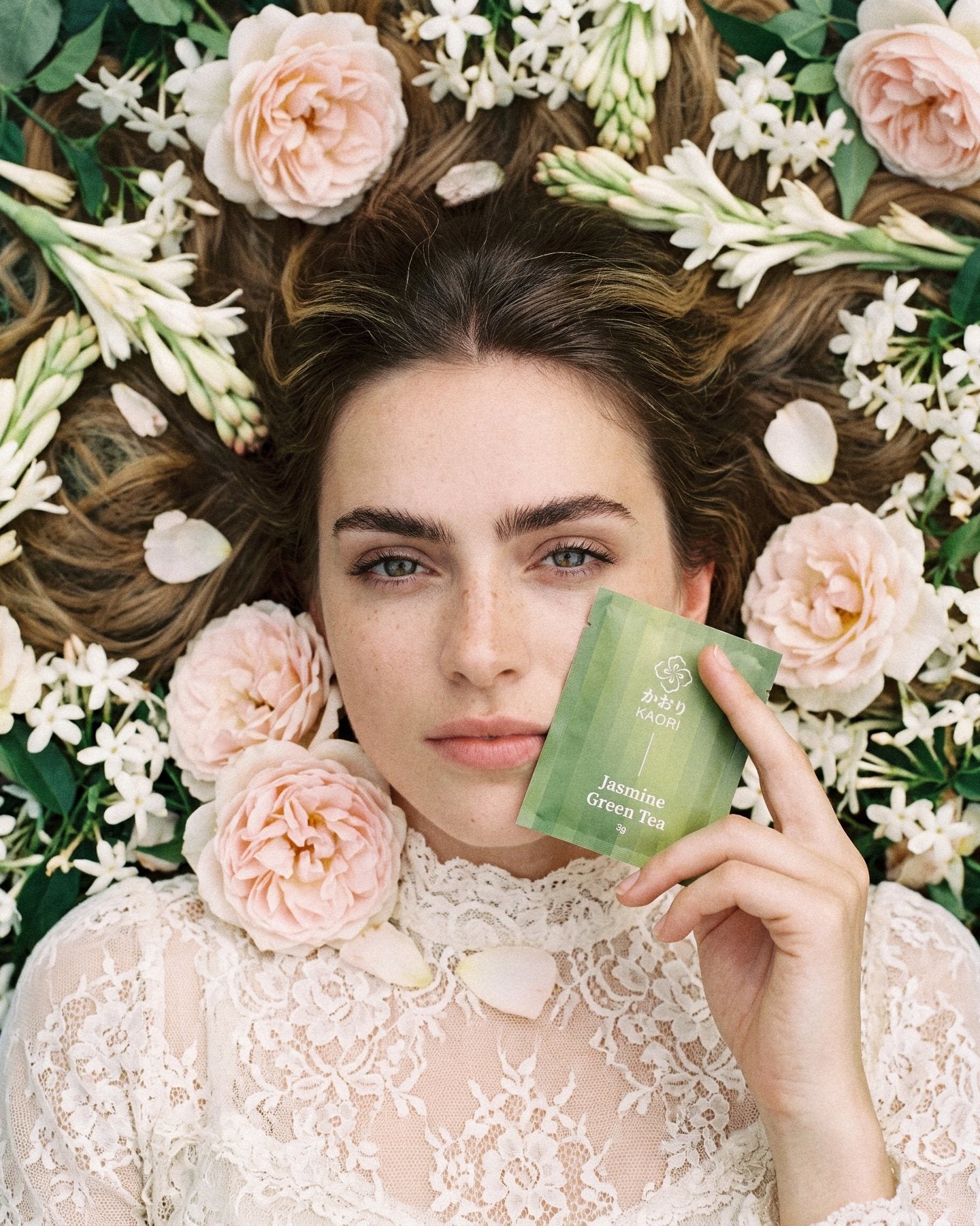 A model in Victorian lace lying among jasmine, tuberose and old roses, a Jasmine Green Tea sachet at her cheek